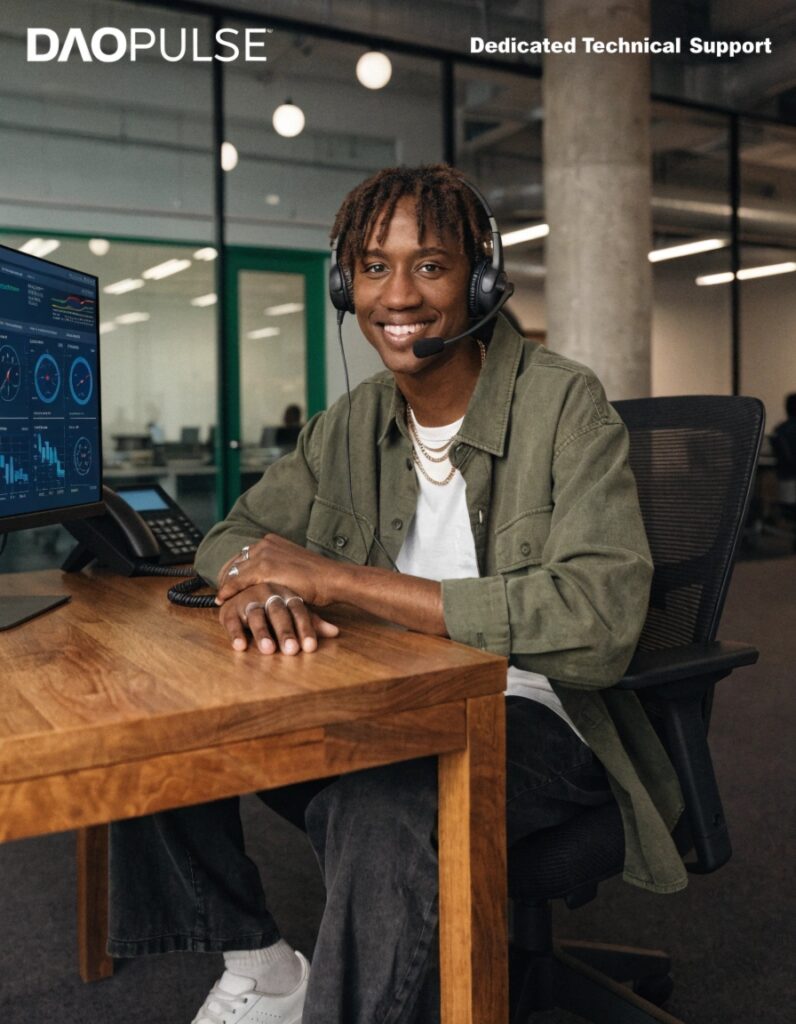 An image of a friendly customer service agent with a headset, in front of a computer showing technical schematics