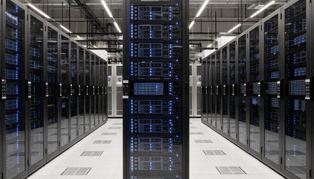 A wide-angle photo of a modern data center showing rows of server racks, with large PDU and cooling units visible